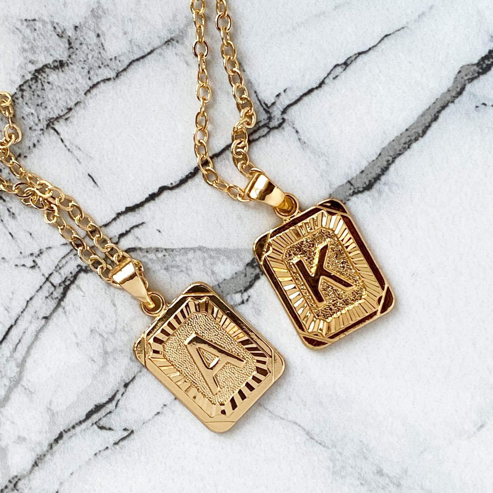 A close up of two initial necklaces on marble.