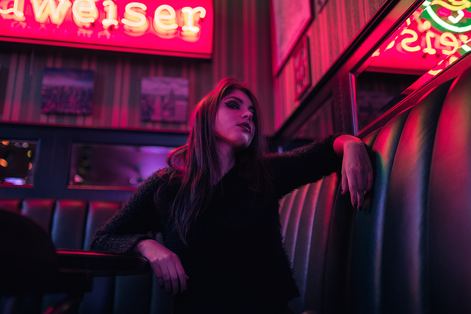 A woman sitting in a diner booth with neon lights behind her.