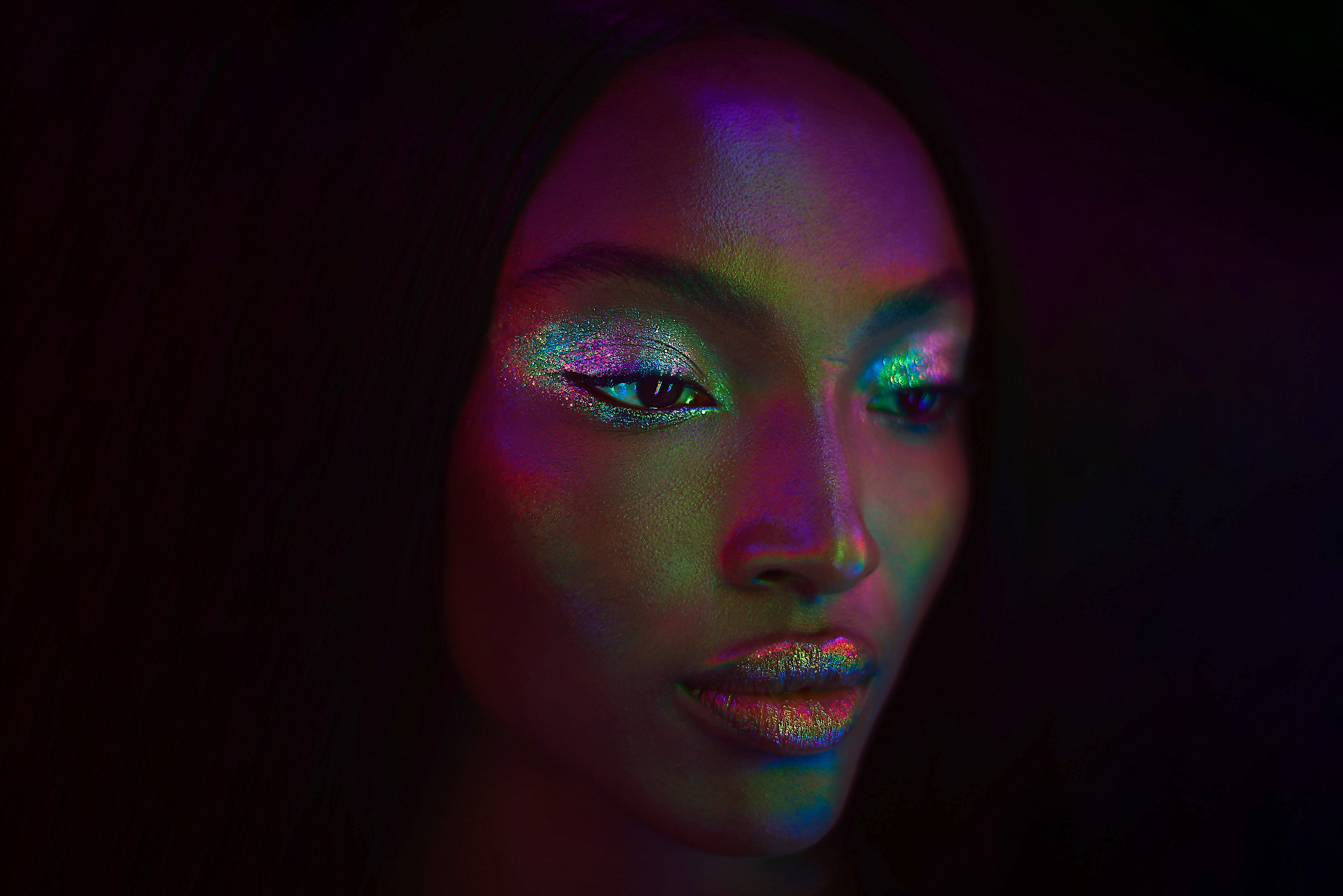 A portrait of a woman with glitter eyeshadow and colorful lighting.
